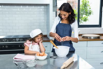 Smiling mother and daughter breaking eggs