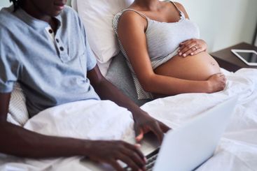 Hands, laptop and pregnancy with couple in bed together...