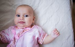 Curious and adorable baby girl in Asian pink attire lying...