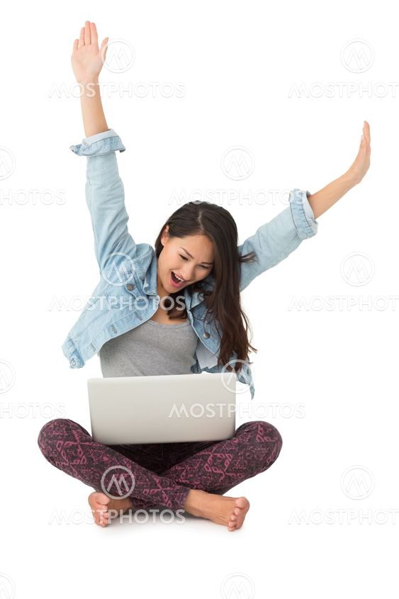 Asian woman cheering with laptop sitting on floor