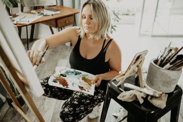 Woman painting in studio with palette, canvas and...