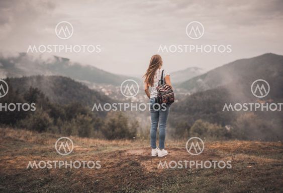 woman standing alone with backpack near mountains