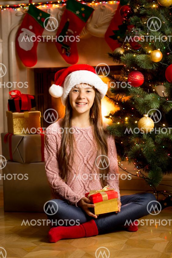 girl in Santa cap on floor with Christmas present at...