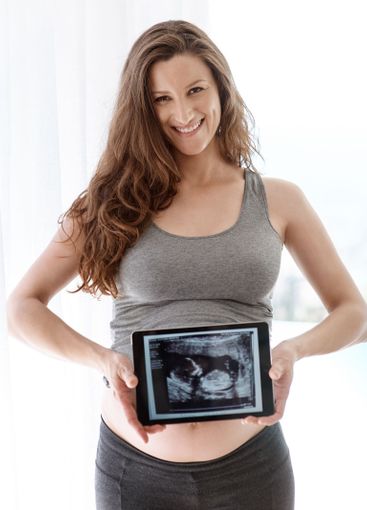 Woman, pregnant and happy with scan on tablet at home...