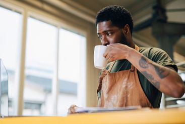 Male baker sipping coffee while working on laptop at bakery