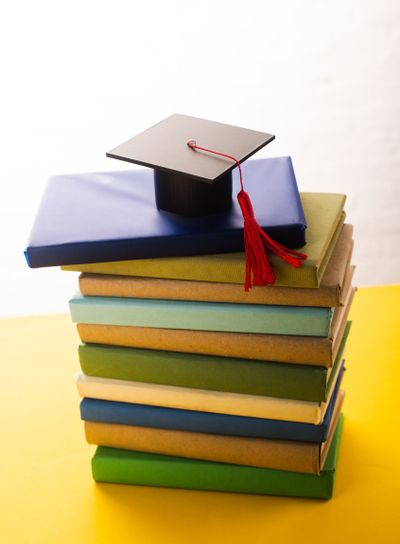 Graduation cap with red tassel on top of books on yellow...