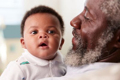 Proud Grandfather Cuddling Baby Grandson In Nursery At Home