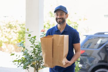 Happy courier man in blue uniform carrying two paper...