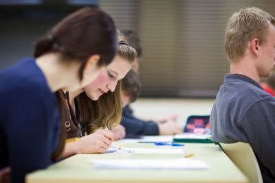 pretty female college student sitting in a classroom full...