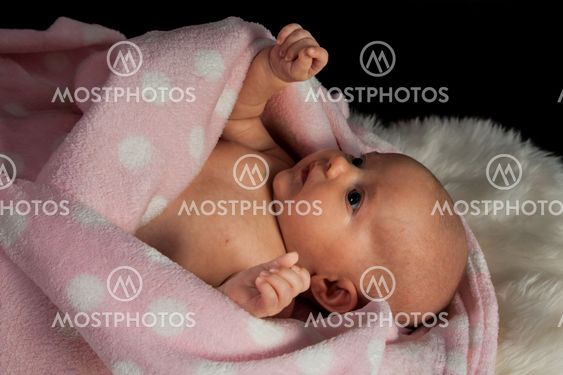 infant wrapped in a blanket on a black background.