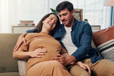 Pregnant woman, man and touch belly on sofa, smile and...