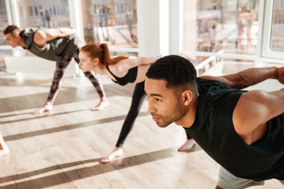 Concentrated african man doing yoga exercises in group at...