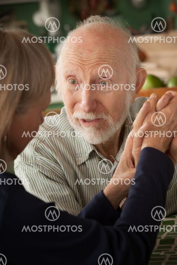 Senior couple at home holding hands focusing on man