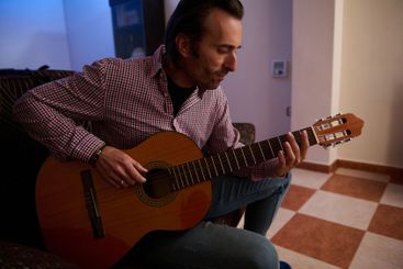 Man playing guitar sitting on a couch in a warm indoor...