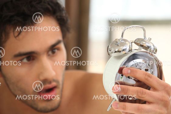 young man looking stunned at alarm clock