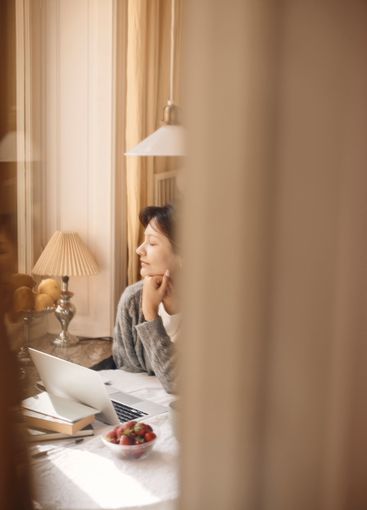 Young woman with hand on chin sitting at table in home