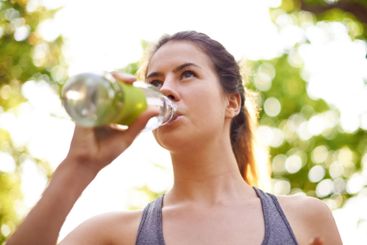 Athlete, fitness and woman drinking water in nature for...