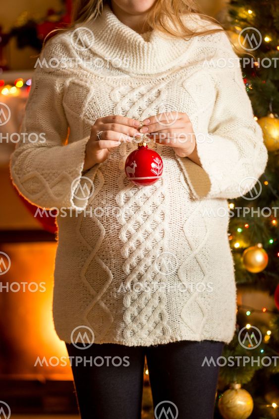pregnant woman posing against fireplace with Christmas ball