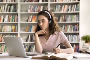 Concentrated young female student wear earphones learn...