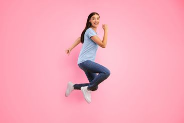 Happy woman jumping over yellow studio wall