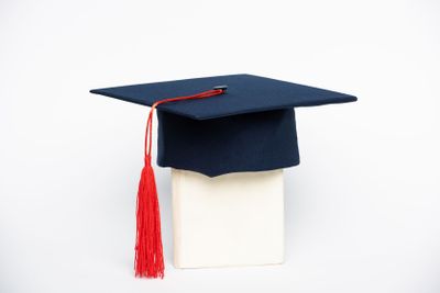 Graduation cap with red tassel on book on white background