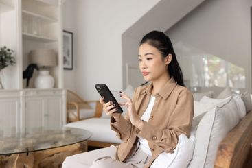 Focused beautiful young adult Asian girl using smart...