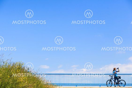 Background for poster or advertisment pertaining to cycling/sport/outdoor activities - female cyclist during a halt on a bridge against blue sky
