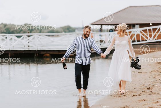 Young spouses go along the beach line barefoot and hold...