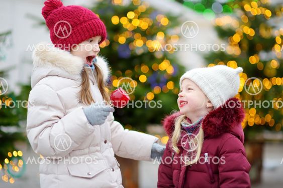 Two adorable little sisters eating red apples covered...