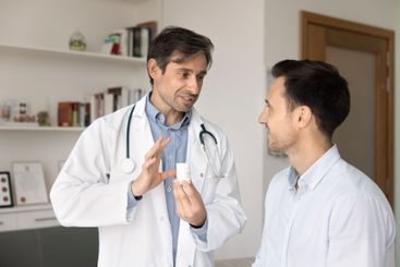 Male doctor showing pills bottle to patient, prescribing...