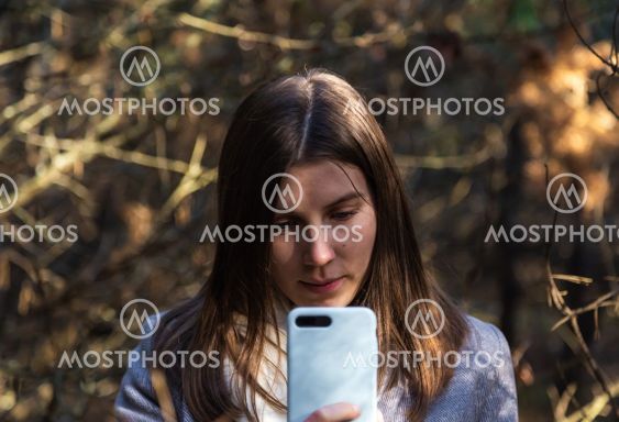 Girl in a gray coat takes a selfie in the forest....