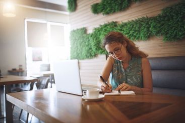 Woman, writing and notebook in cafe with remote work,...