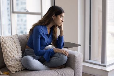 Woman sitting by window looking outside with pensive...
