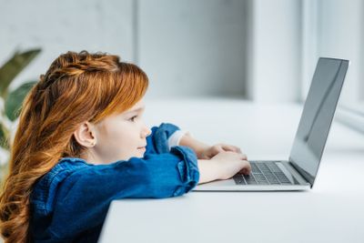 Cute redhead child using laptop by window