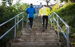 Two athletes running on stairs in sunny autumn, rear view.