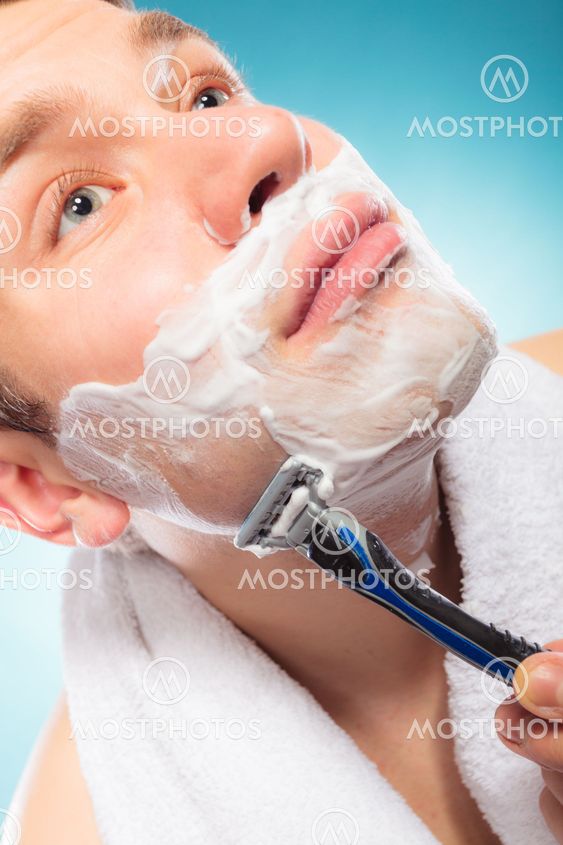 Young man shaving using razor with cream foam.