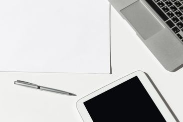 Workspace with laptop, notepad, tablet, and pen arranged...