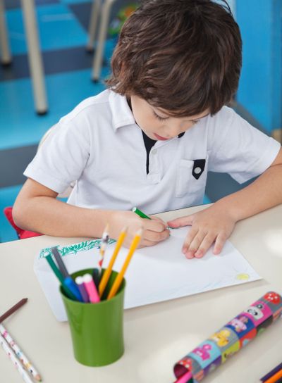 Little Boy Drawing At Desk In Art Class