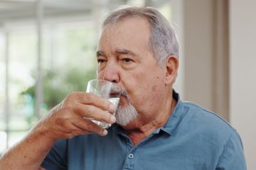 Senior man, drinking water and medicine in home for...