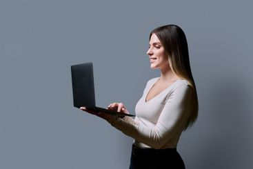 Profile view, young woman using laptop on grey studio...