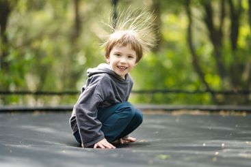Little boy jumping on a trampoline in a backyard on warm...
