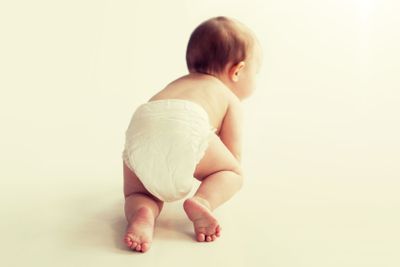 little baby in diaper crawling on white floor