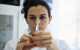 A focused nurse in a white lab coat carefully prepares a...