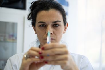 A focused nurse in a white lab coat carefully prepares a...