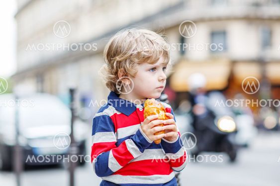 Little cute child on a street of city eating fresh croissant
