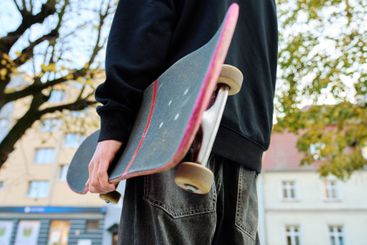 Skateboarder holding worn skateboard walks at street