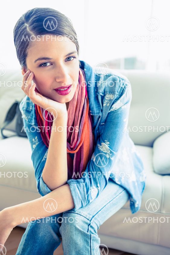 Pretty brunette sitting on sofa smiling at camera