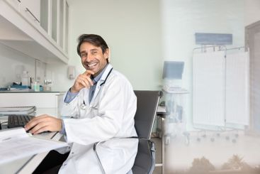 Portrait of happy successful male doctor sitting at...