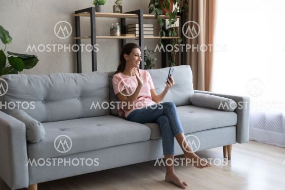 Smiling Arabian woman holding smartphone, waving hand,...