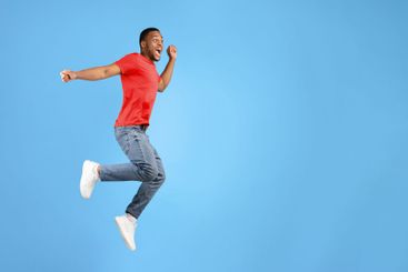 Joyful African Man Jumping And Shouting In Mid-Air, Blue...